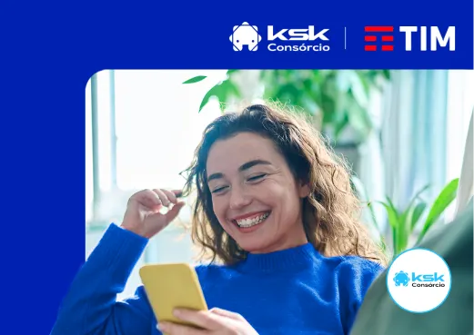 Consórcio KSK e TIM, mulher jovem sorri enquanto usa o celular sentada no sofá da sala